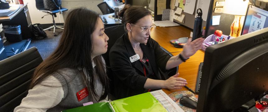 Student and staff member view a computer screen while engaged in discussion 
